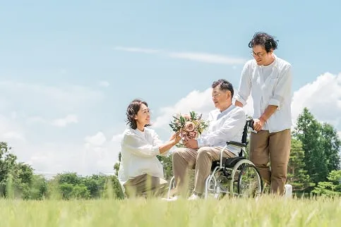 草原で車椅子の男性に花束を渡す女性
